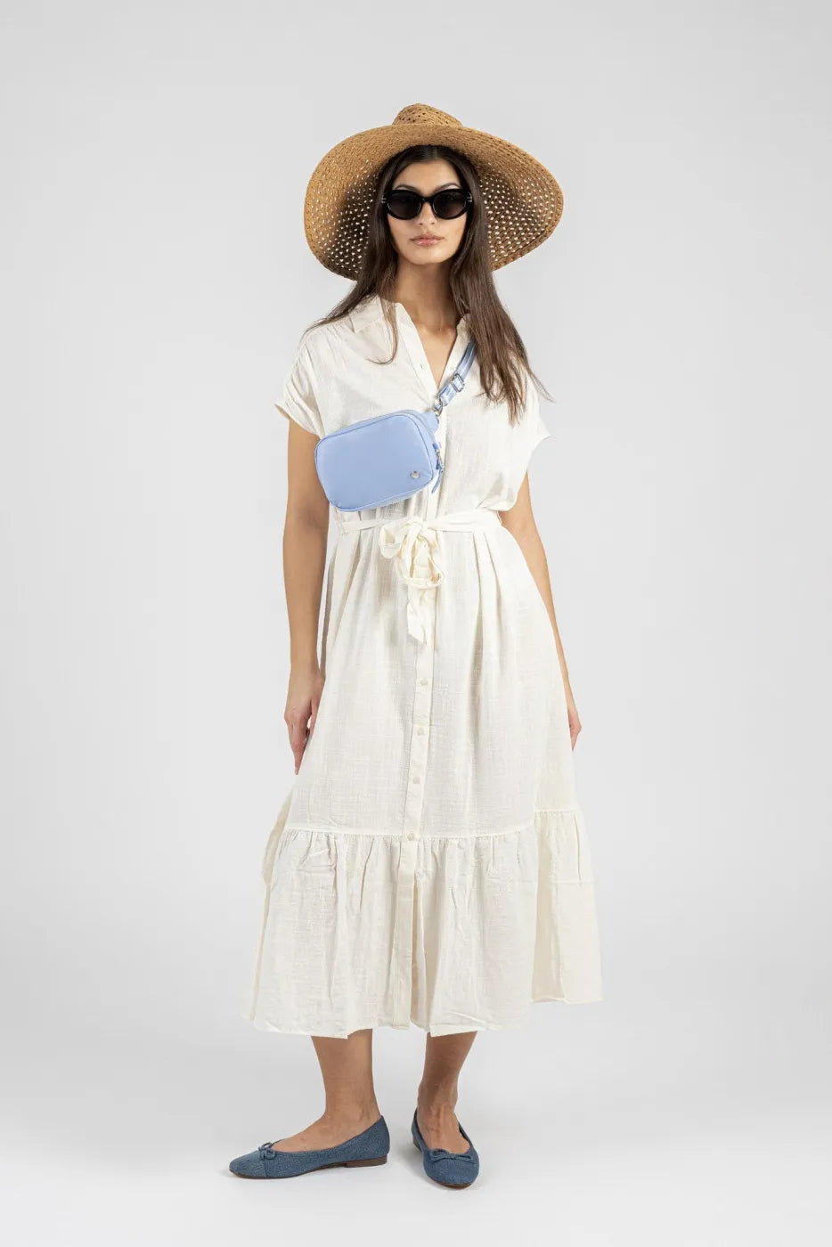 Pacsafe W Anti-theft Micro Sling in Serenity Blue, worn at the waist by a woman in a cream dress, seen from the front