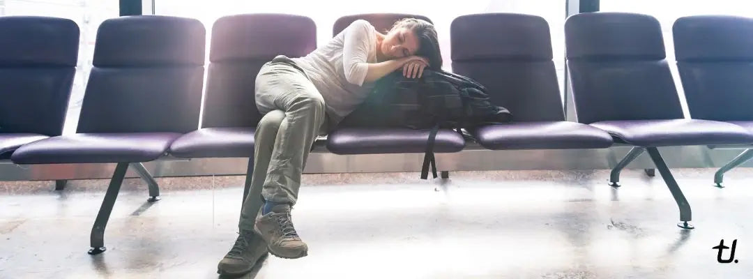 Tired traveller sleeping across airport seats while waiting for a long-haul flight