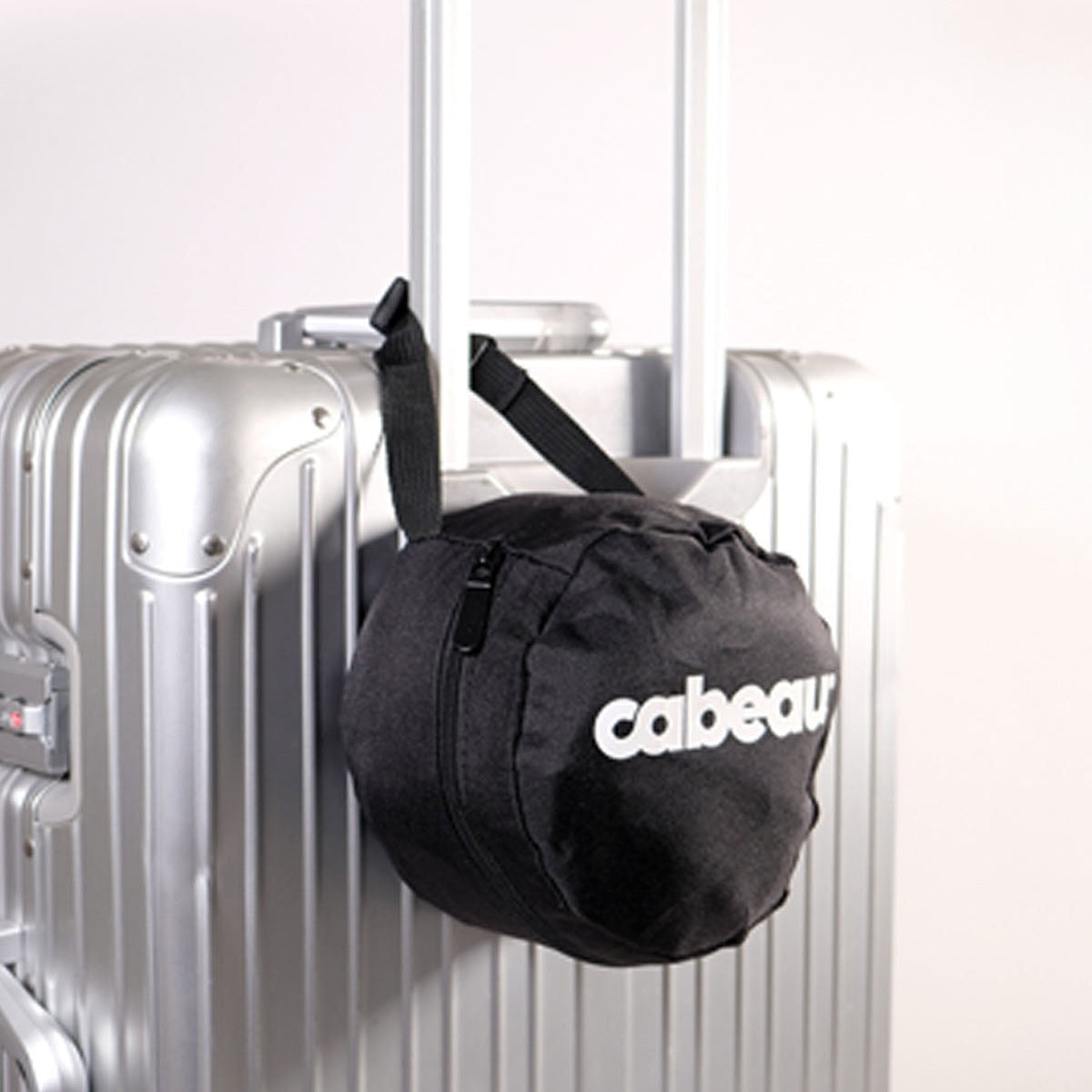 Compact  Cabaeau travel carry bag attached to a silver suitcase against a white background