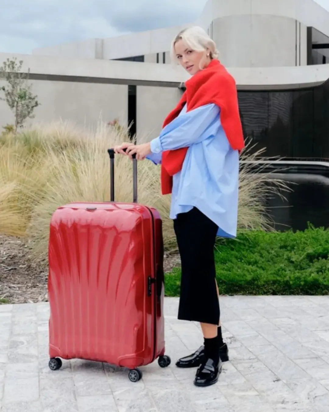 Woman pulling a red Samsonite C-Lite suitcase outdoors near modern architecture