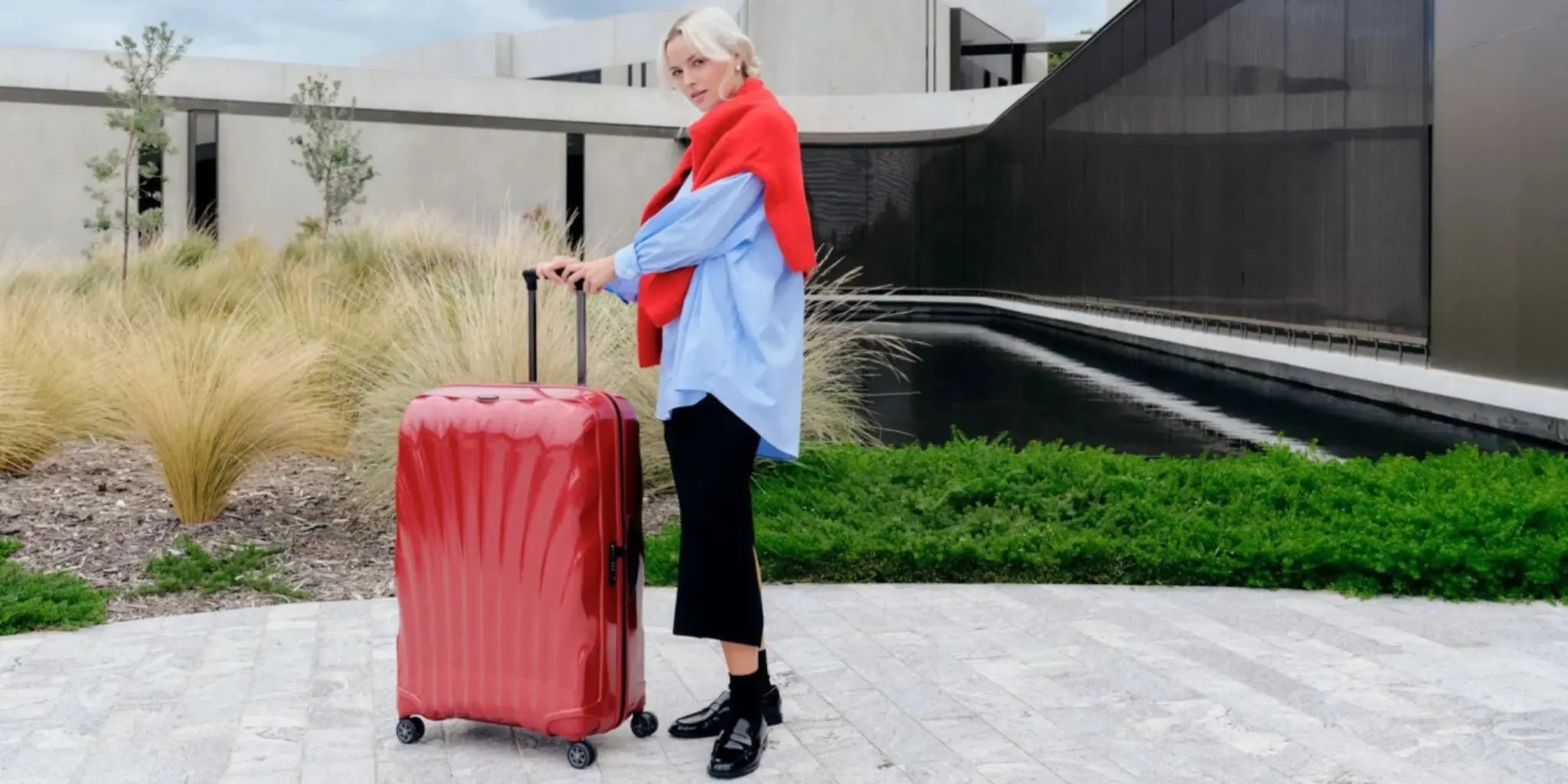 Woman pulling a red Samsonite C-Lite suitcase outdoors near modern architecture