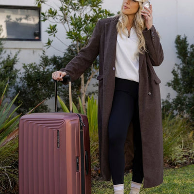 Woman in a brown coat with a medium suitcase outdoors