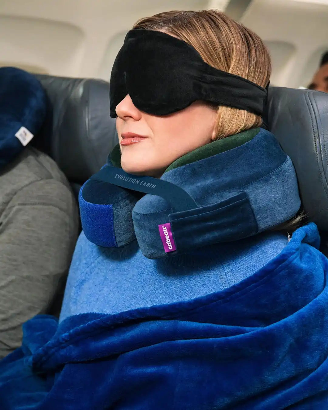 Person using a Cabeau travel pillow, blanket and eye mask on an airplane