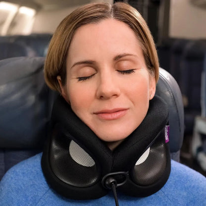 A woman with her eyes closed rests her neck on a Cabeau Evolution X travel neck pillow while seated in a plane cabin. 