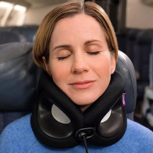 A woman with her eyes closed rests her neck on a Cabeau Evolution X travel neck pillow while seated in a plane cabin. 