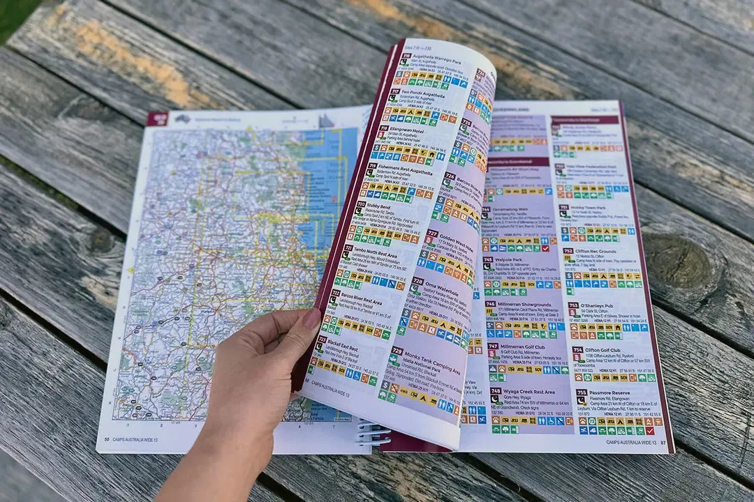 Open camps australia wide 13 guidebook with colorful index and map spread on wooden table for australia wide camping trips