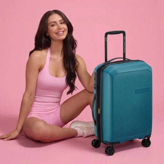 girl sits next to a Delsey Anvers 55 cm 4 Wheel Expandable Carry-on Suitcase - Teal