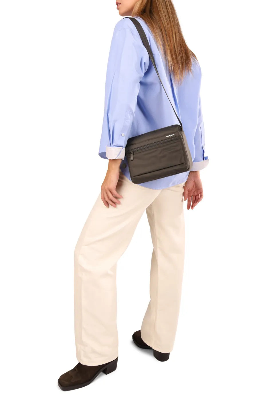 Hedgren EYE Crossbody Bag with RFID Pocket in Black, worn crossbody at the waist over a blue shirt and cream trousers