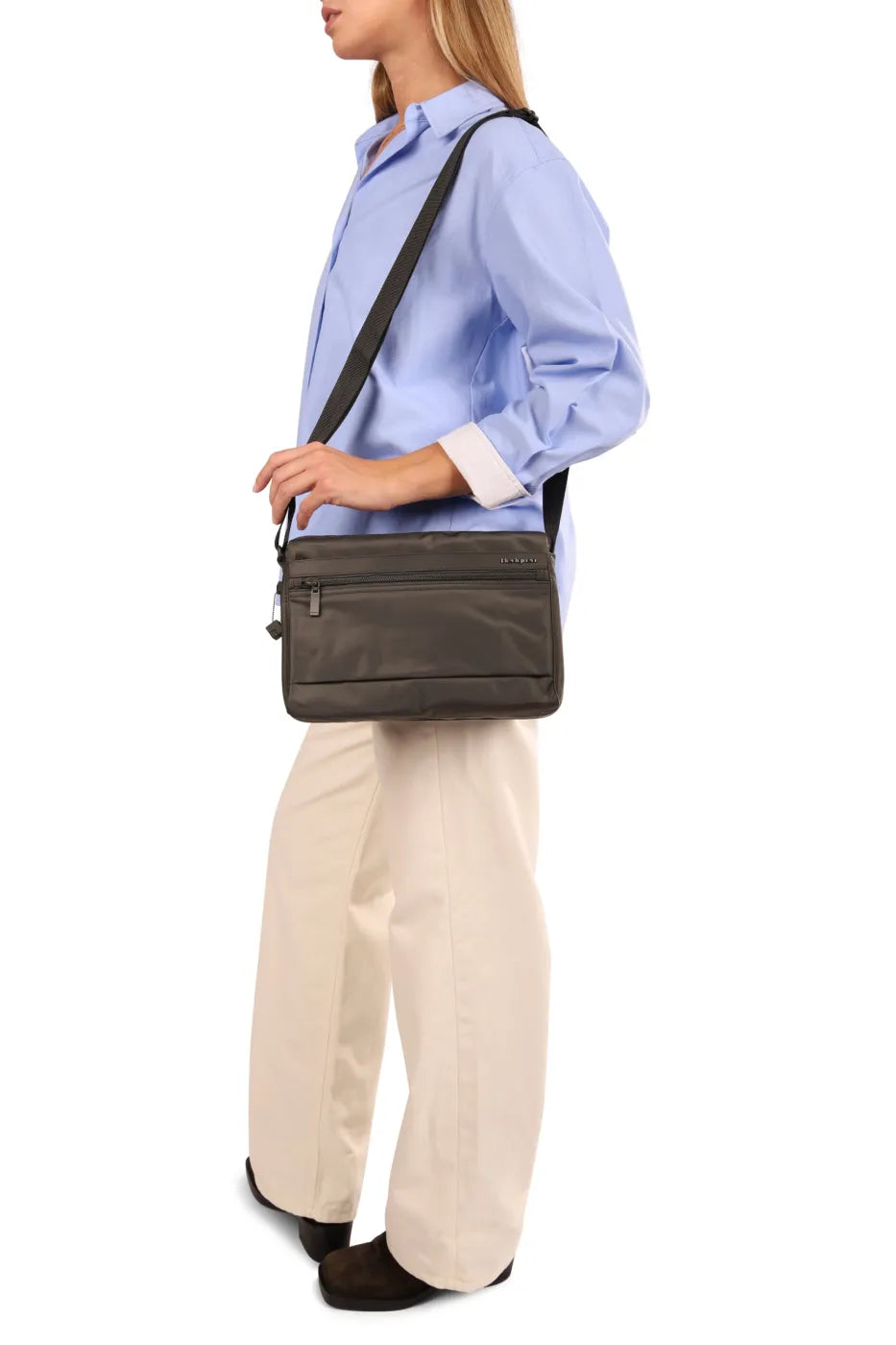 Hedgren EYE NEO Medium Crossbody Bag with RFID Pocket in Willow Grey, worn crossbody at the hip by a woman in a blue shirt, seen from the side