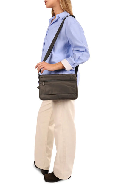 Hedgren EYE NEO Medium Crossbody Bag with RFID Pocket in Willow Grey, worn crossbody at the hip by a woman in a blue shirt, seen from the side
