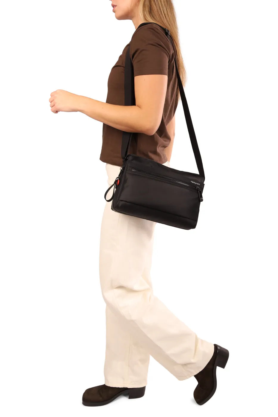 Hedgren EYE NEO Medium Crossbody Bag with RFID Pocket in Willow Grey, worn crossbody at the hip by a woman in a brown tee and cream trousers