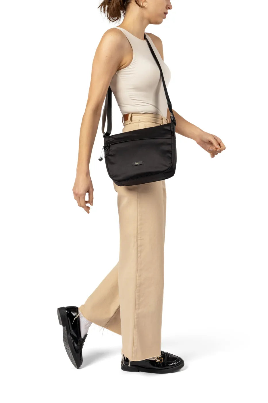 Hedgren GRAVITY Medium Crossover Shoulder Bag in Black, worn crossbody at the hip by a woman in a white tank and tan trousers