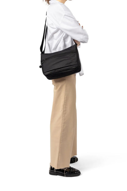 Hedgren HARPER'S NEO Small Crossbody Bag with RFID in Dahlia Red, worn crossbody at the hip by a woman in a white shirt and tan trousers