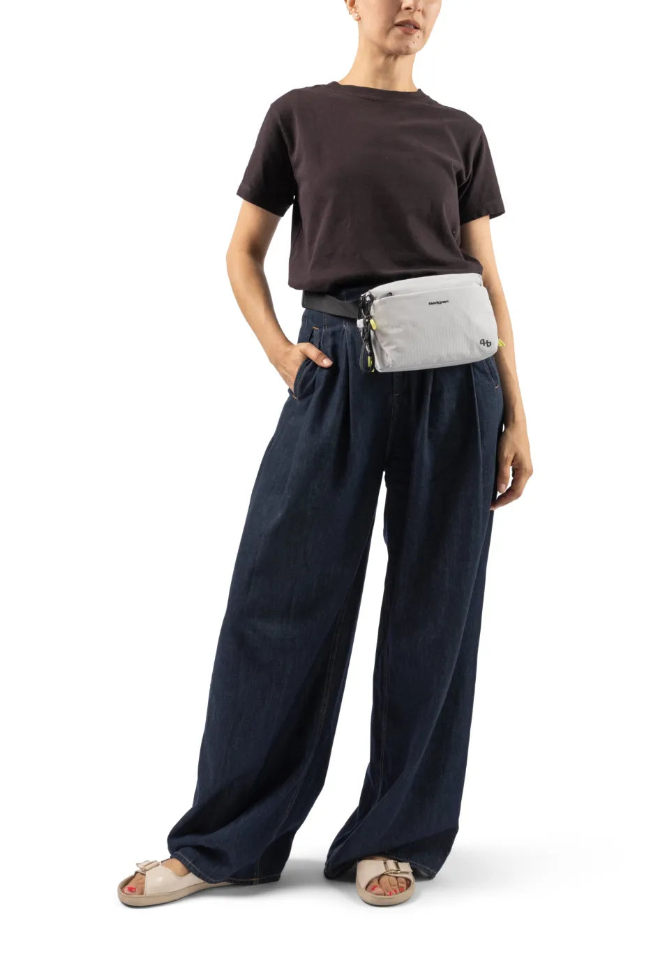 Hedgren JUN Waistbag in Vulcan Blue, worn at the front of the waist by a woman in a dark tee and wide denim trousers