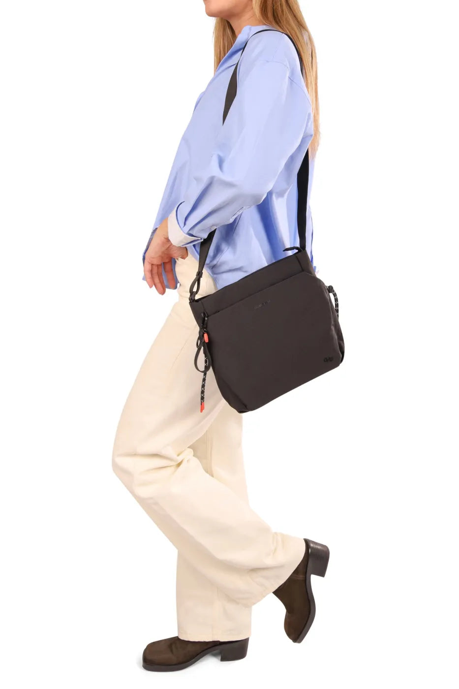 Hedgren MAKOTO Square Crossover Bag in Vulcan Blue, worn crossbody at the hip by a woman walking in a blue shirt and cream trousers