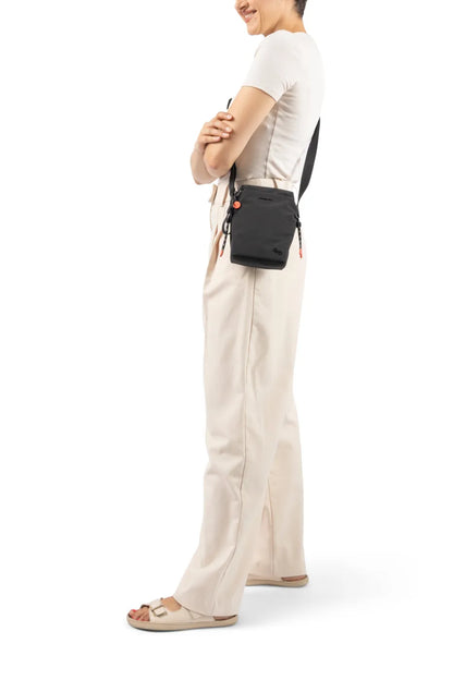 Hedgren SIPHO Phone/Bottle Bag in Vulcan Blue, worn crossbody at the hip by a woman in a white tee and cream trousers