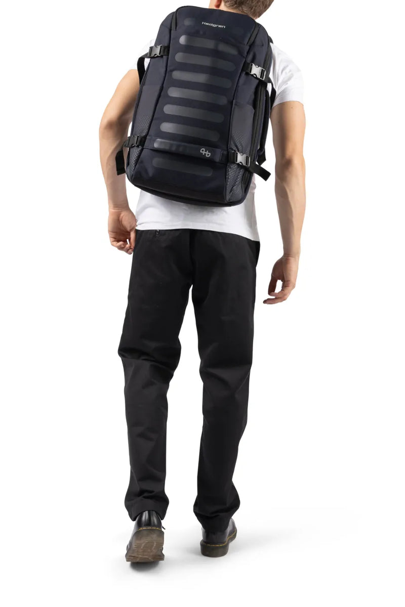 Hedgren TRIP L Expandable 15.6" Laptop Travel Backpack with RFID in Black, worn on both shoulders by a man in a white tee, seen from behind
