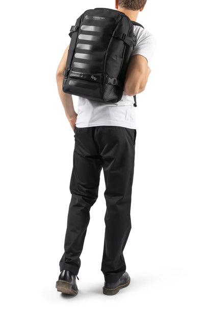 Hedgren TRIP M Expandable 15.6" Laptop Travel Backpack with RFID in Black, worn on both shoulders by a man in a white tee, seen from behind