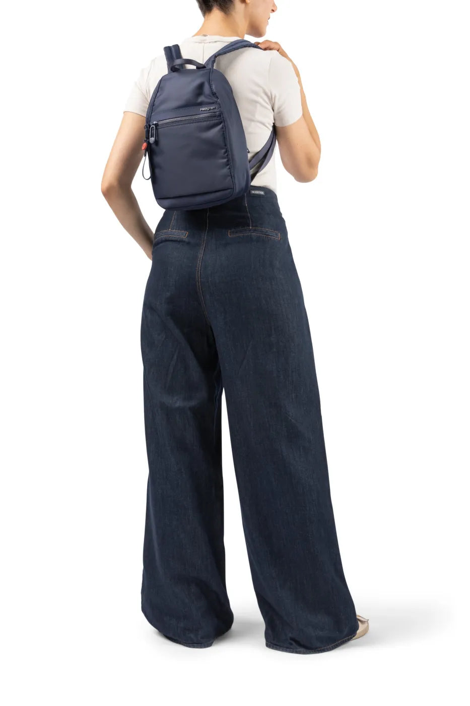 Hedgren VOGUE Small Backpack in Dahlia Red, swung onto one shoulder by a woman in wide denim trousers