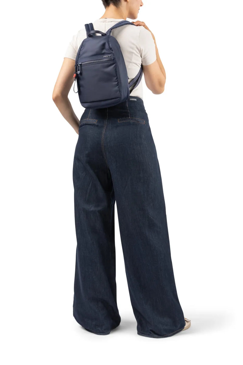 Hedgren VOGUE Small Backpack in Dahlia Red, swung onto one shoulder by a woman in wide denim trousers