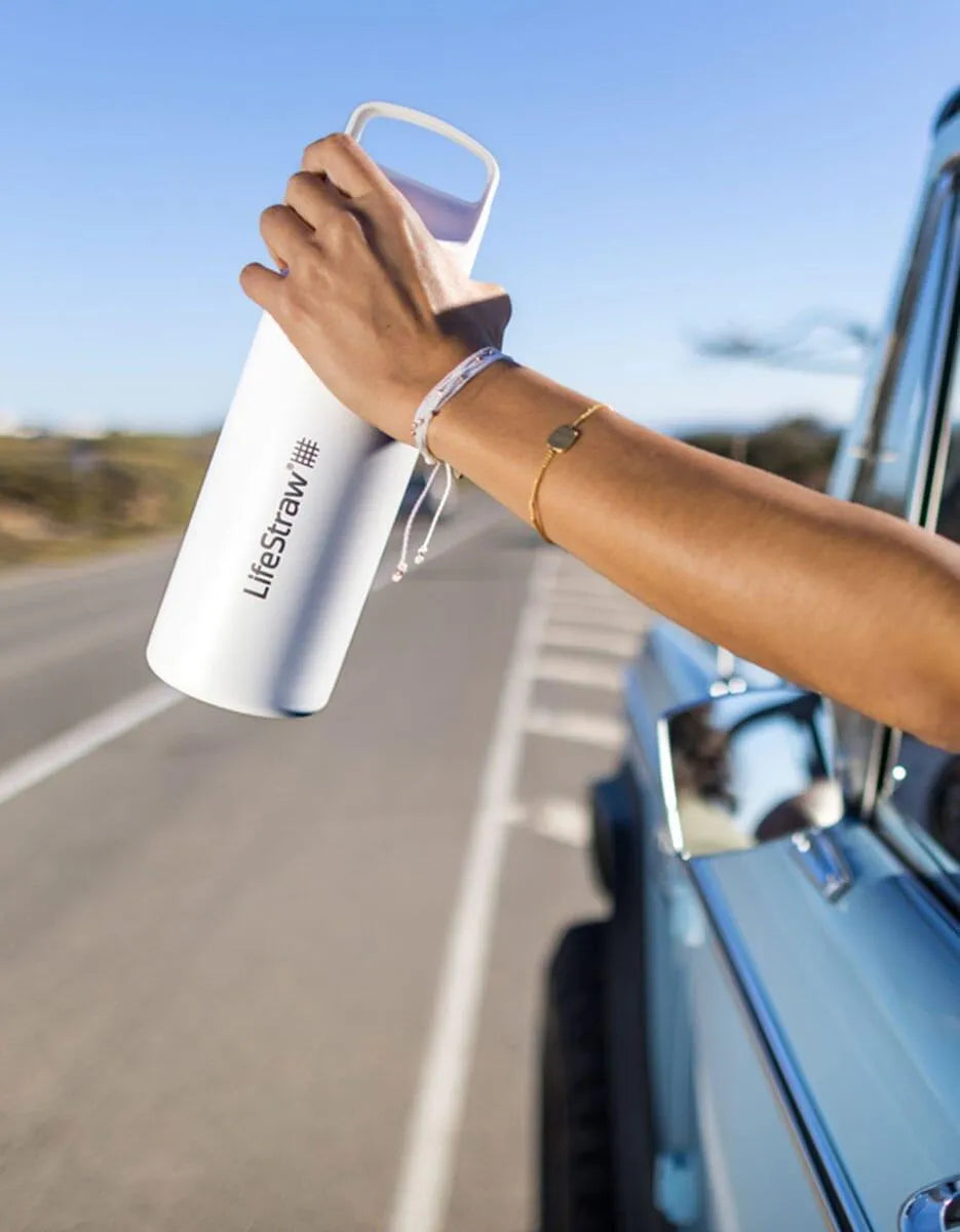 LifeStraw Go 2.0: a white stainless steel LifeStraw Go bottle held out of a car window on an open road
