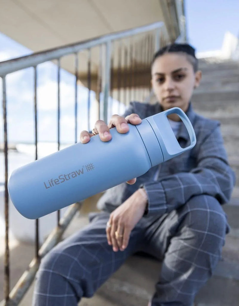 LifeStraw Go 2.0: a light blue stainless steel LifeStraw Go bottle held out by a woman sitting on concrete steps
