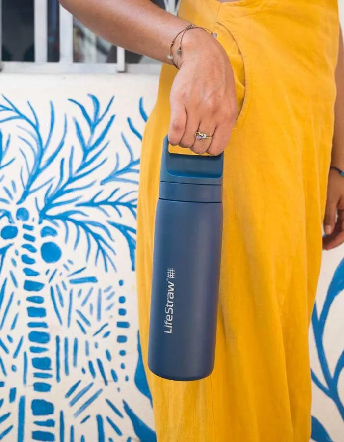 LifeStraw Go 2.0: a navy LifeStraw Go 500ml stainless steel bottle carried by its handle beside a yellow skirt