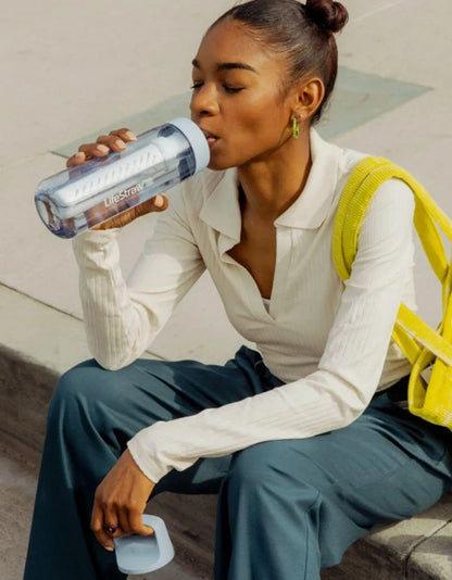 LifeStraw Go 2.0: a woman sitting on a kerb drinking from a light blue LifeStraw Go bottle