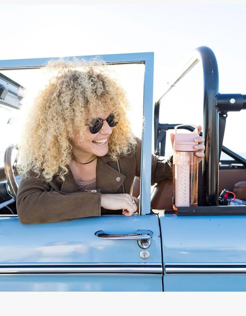 LifeStraw Go 2.0: a woman smiling from the window of a vintage blue car with a pink LifeStraw Go bottle