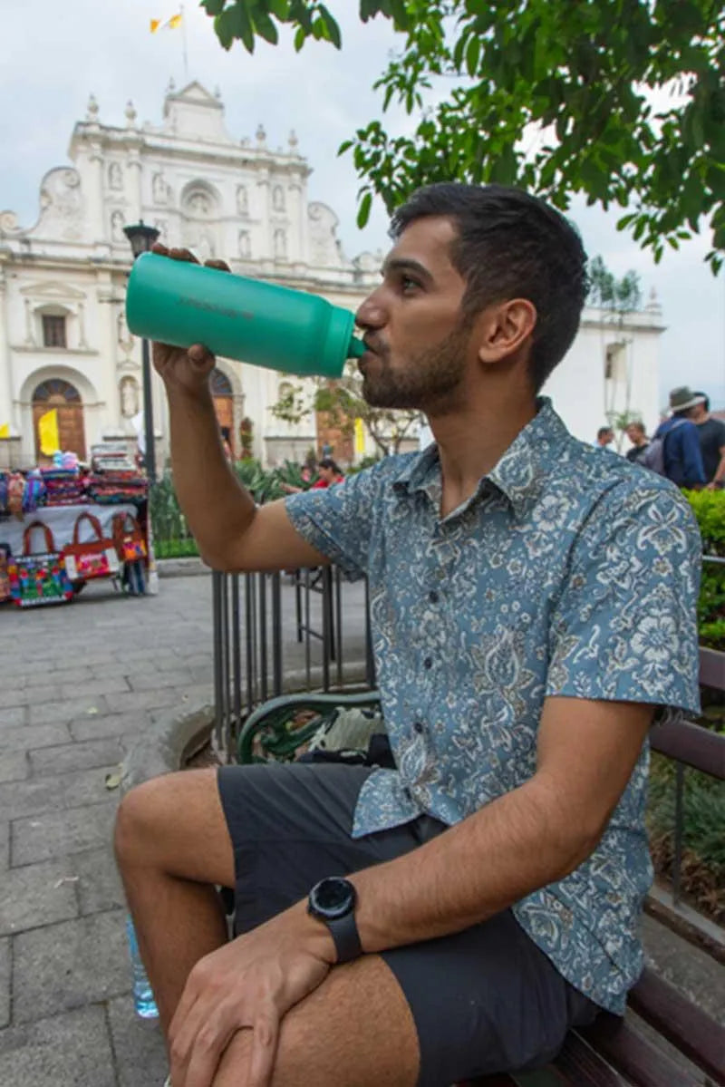LifeStraw Go 2.0: a man drinking from a green stainless steel LifeStraw Go bottle on a bench in a town square