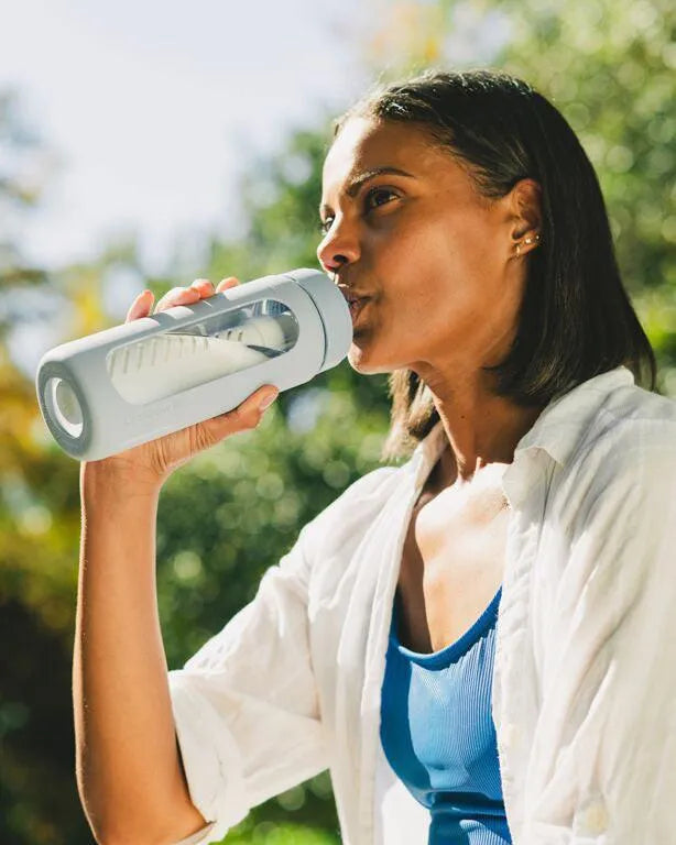LifeStraw Go Glass 590ml Water Filter Bottle: a woman drinking from a LifeStraw Go Glass bottle in Icelandic Blue outdoors in the sun