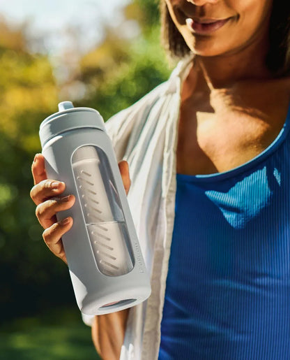 LifeStraw Go Glass 590ml Water Filter Bottle: a woman in a blue top holding a LifeStraw Go Glass bottle in Icelandic Blue in a sunny garden