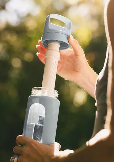 LifeStraw Go Glass 590ml Water Filter Bottle: hands lifting the lid and filter out of a LifeStraw Go Glass bottle in Icelandic Blue outdoors