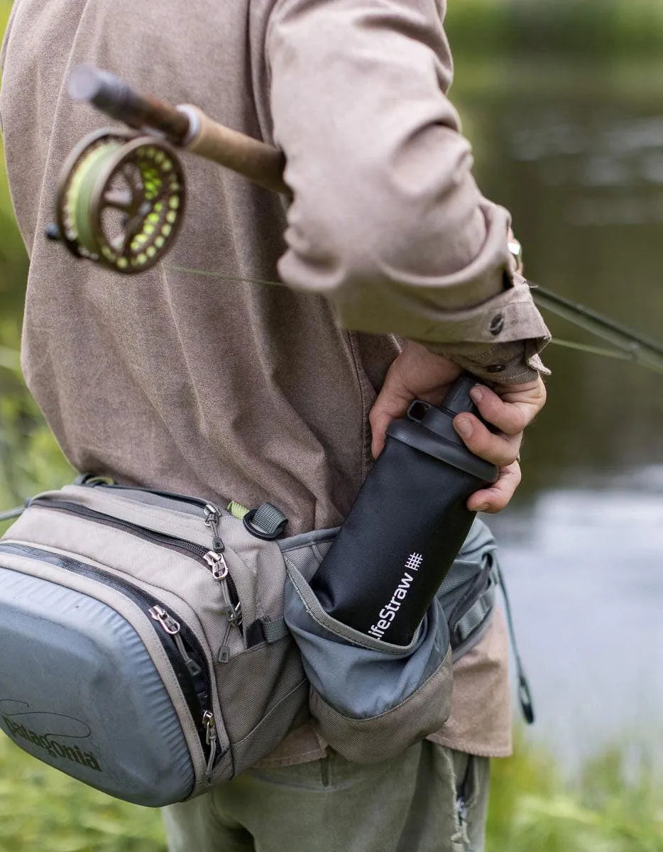 LifeStraw Peak 650ml Collapsible Squeeze Bottle with Filter: an angler tucking a dark grey LifeStraw Peak squeeze bottle into a hip pack beside a river