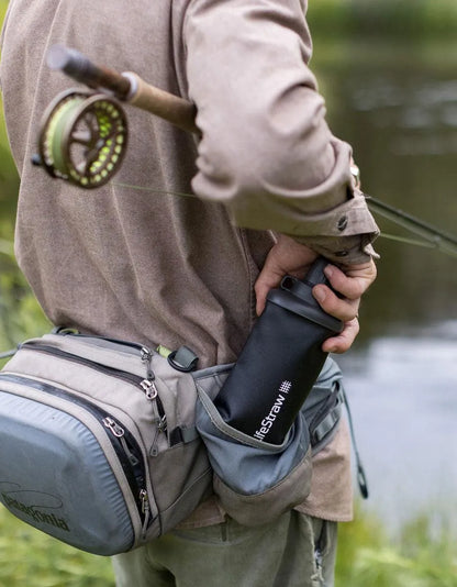 LifeStraw Peak 650ml Collapsible Squeeze Bottle with Filter: an angler tucking a dark grey LifeStraw Peak squeeze bottle into a hip pack beside a river