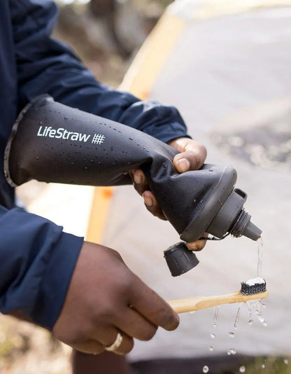 LifeStraw Peak 650ml Collapsible Squeeze Bottle with Filter: a dark grey LifeStraw Peak squeeze bottle rolled up to squeeze water out at a campsite