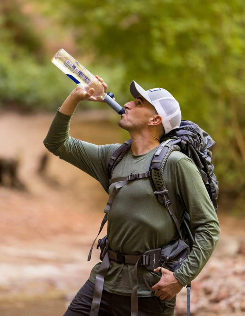 LifeStraw Peak Solo Water Filter: a hiker with a backpack drinking through a LifeStraw Peak Solo from a bottle beside a creek