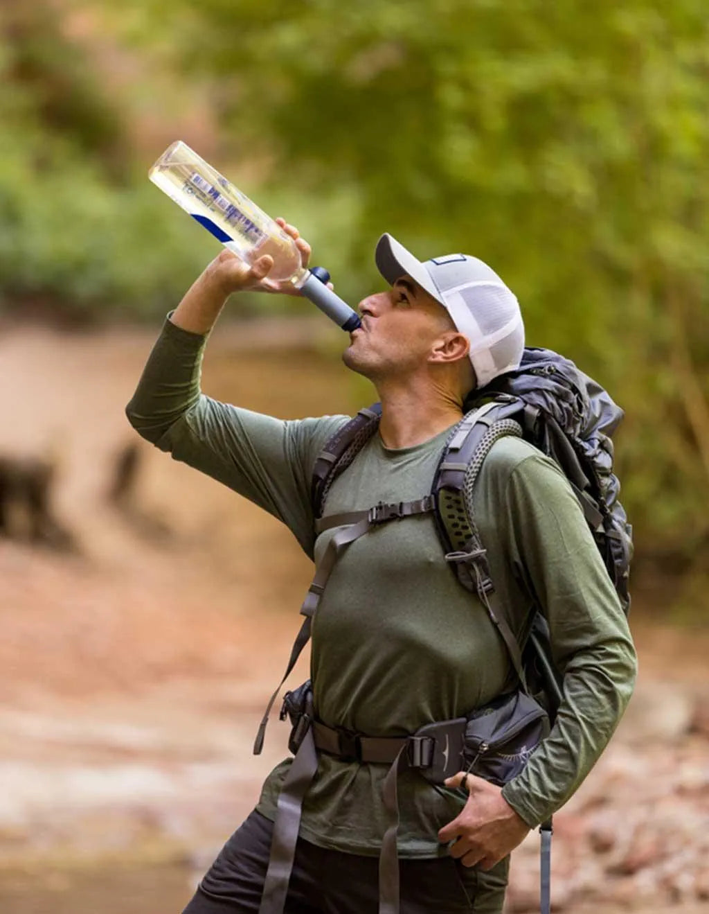 LifeStraw Peak Solo Water Filter: a hiker with a backpack drinking through a LifeStraw Peak Solo from a bottle beside a creek