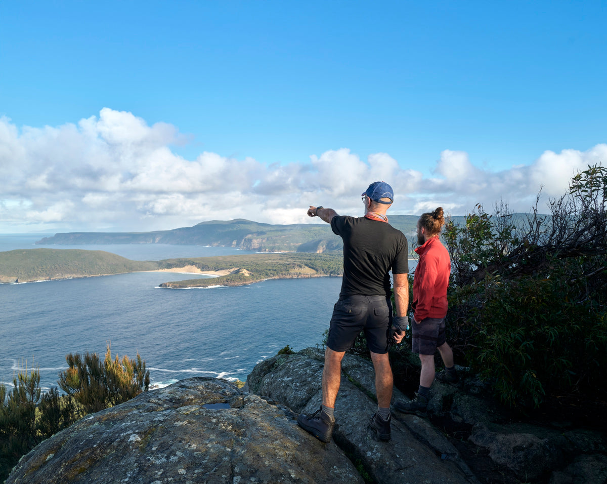 Two hikers on a rocky lookout pointing across the bay on the Three Capes Track, Tasmania