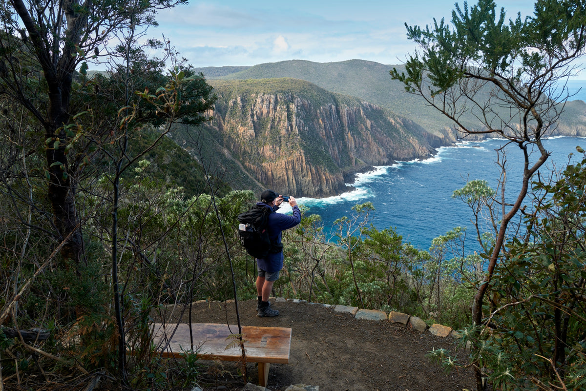 Hiker photographing the sea cliffs from a lookout on the Three Capes Track
