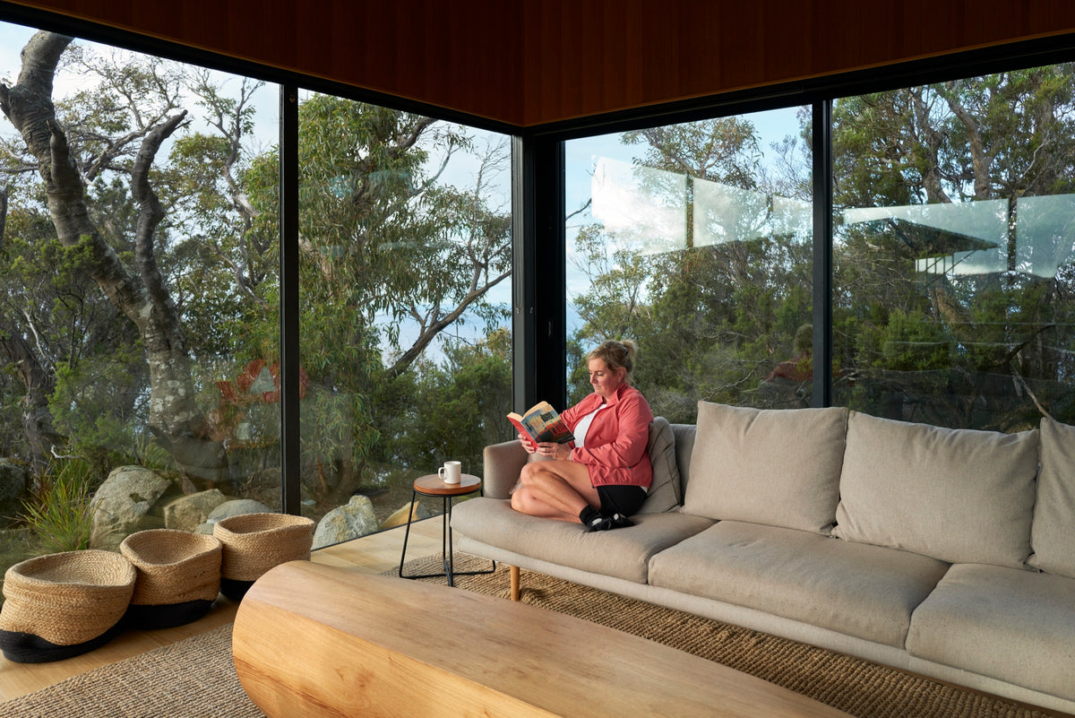 Guest reading in the glass-walled lounge of a Three Capes lodge