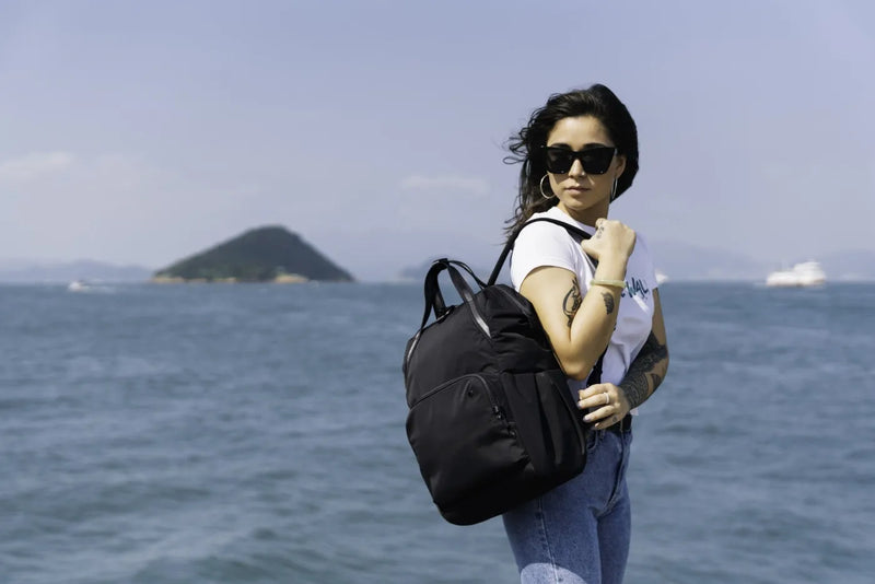 Pacsafe Citysafe CX Anti-Theft 16" Laptop Backpack in Black, carried on one shoulder by a woman at the water's edge