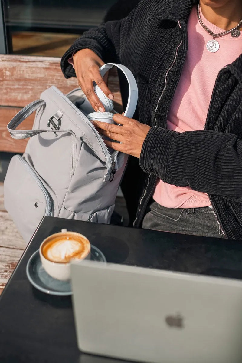 Pacsafe Citysafe CX Anti-Theft 16" Laptop Backpack in Gravity Grey, headphones being packed into the top of the bag at a cafe table