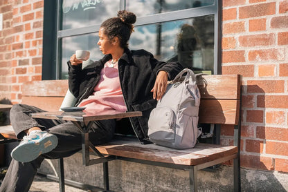 Pacsafe Citysafe CX Anti-Theft 16" Laptop Backpack in Gravity Grey, beside a woman having coffee on a bench outside a cafe