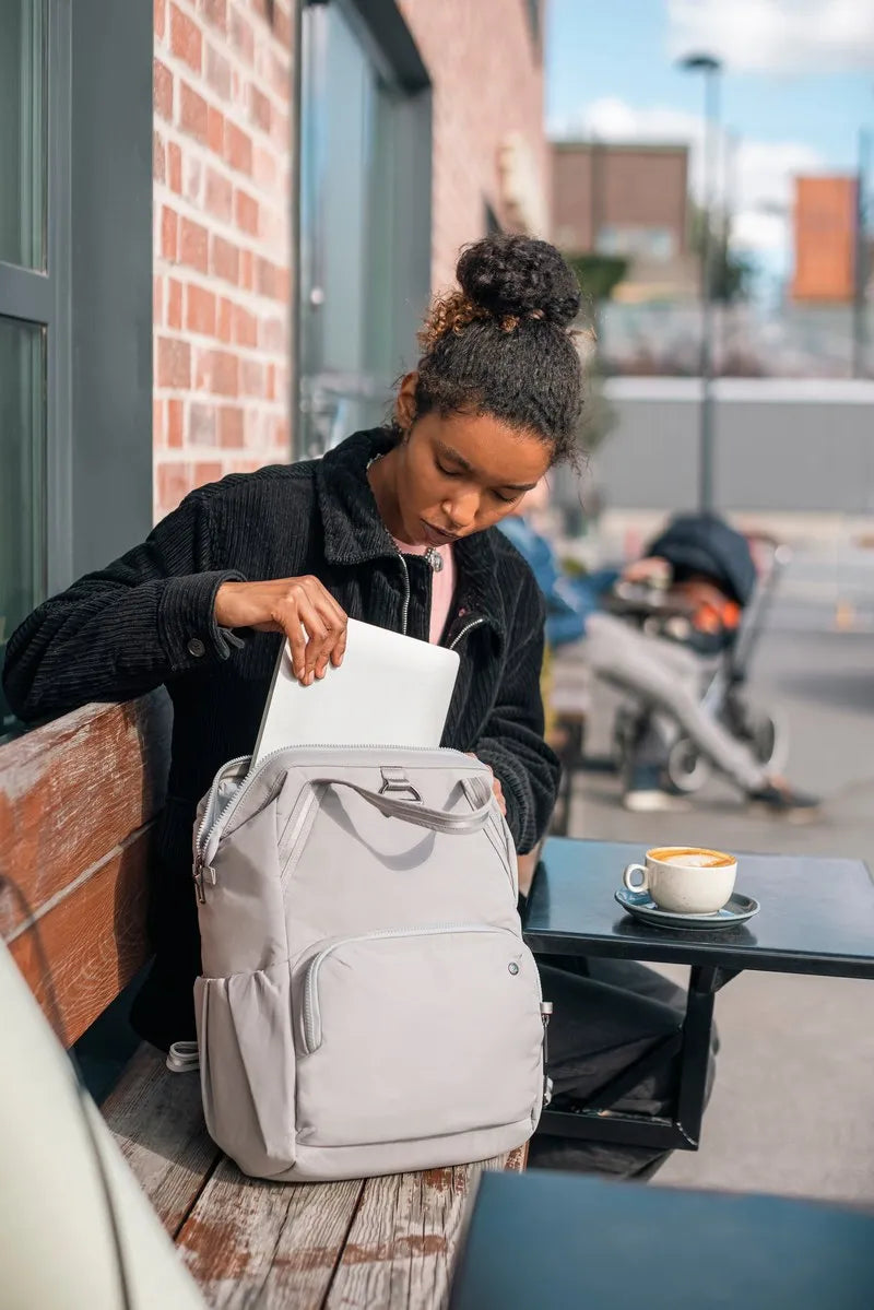 Pacsafe Citysafe CX Anti-Theft 16" Laptop Backpack in Gravity Grey, a laptop being lifted out at an outdoor cafe table