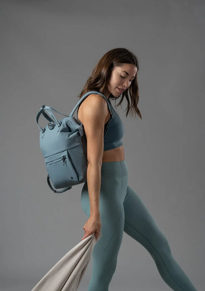 Pacsafe Citysafe CX Econyl Anti-Theft Mini Backpack in Fresh Mint, worn on both shoulders by a woman walking, seen from the side