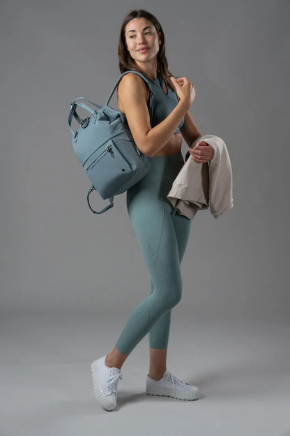 Pacsafe Citysafe CX Econyl Anti-Theft Mini Backpack in Fresh Mint, worn on one shoulder by a woman carrying a sweatshirt