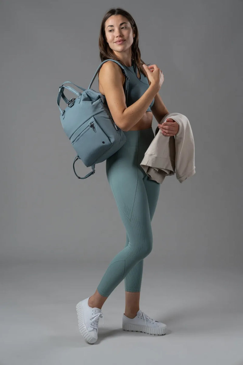 Pacsafe Citysafe CX Econyl Anti-Theft Mini Backpack in Fresh Mint, worn on one shoulder by a woman carrying a sweatshirt