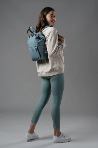Pacsafe Citysafe CX Econyl Anti-Theft Mini Backpack in Fresh Mint, worn on both shoulders by a woman looking back over her shoulder
