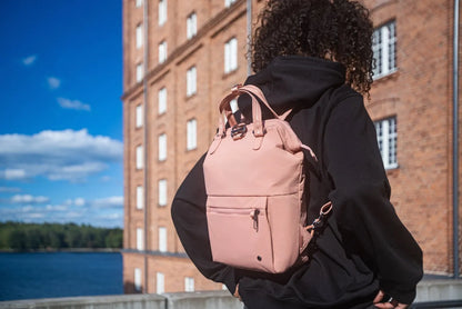 Pacsafe Citysafe CX Econyl Anti-Theft Mini Backpack in Rose, worn on one shoulder by a woman on a waterfront terrace